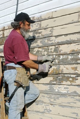 man scraping exterior paint from house