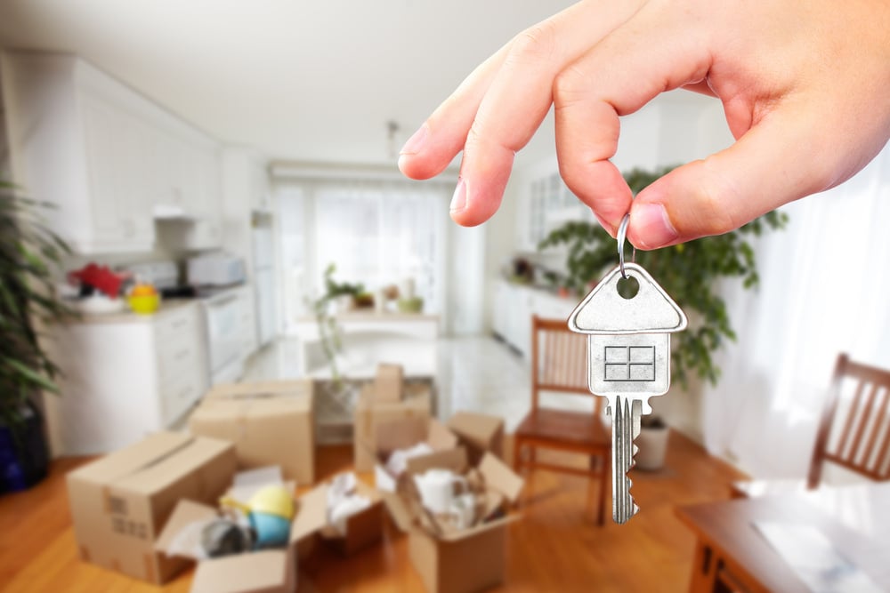 hand holding house key with moving boxes in background