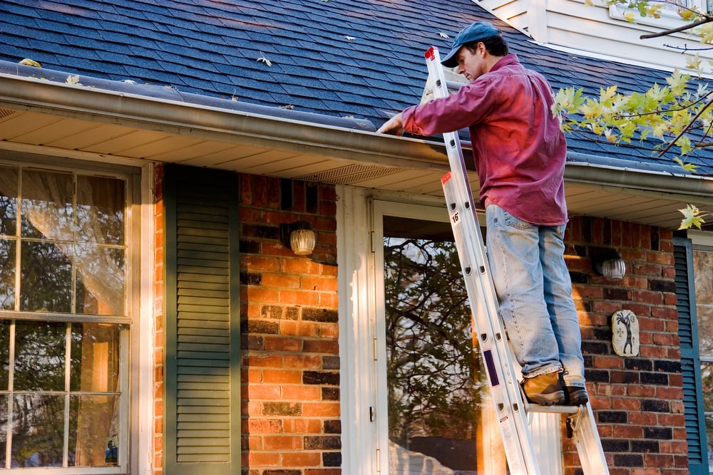 man on ladder cleaning gutters