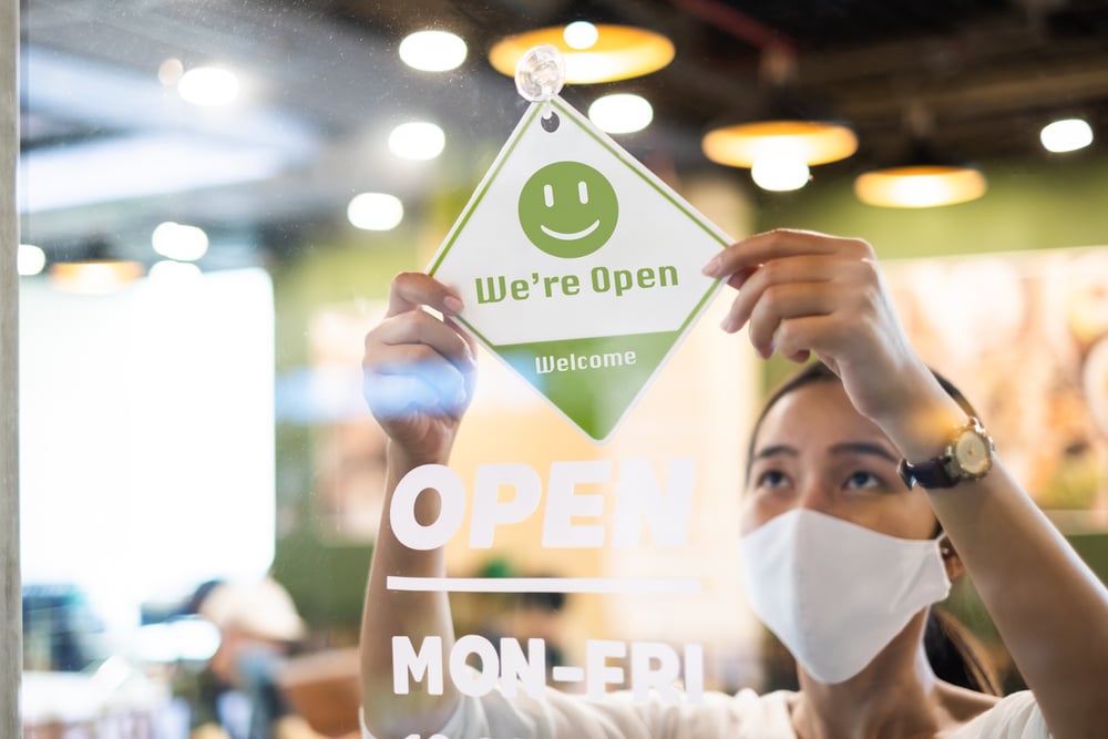 Asian woman wearing mask hanging up open sign