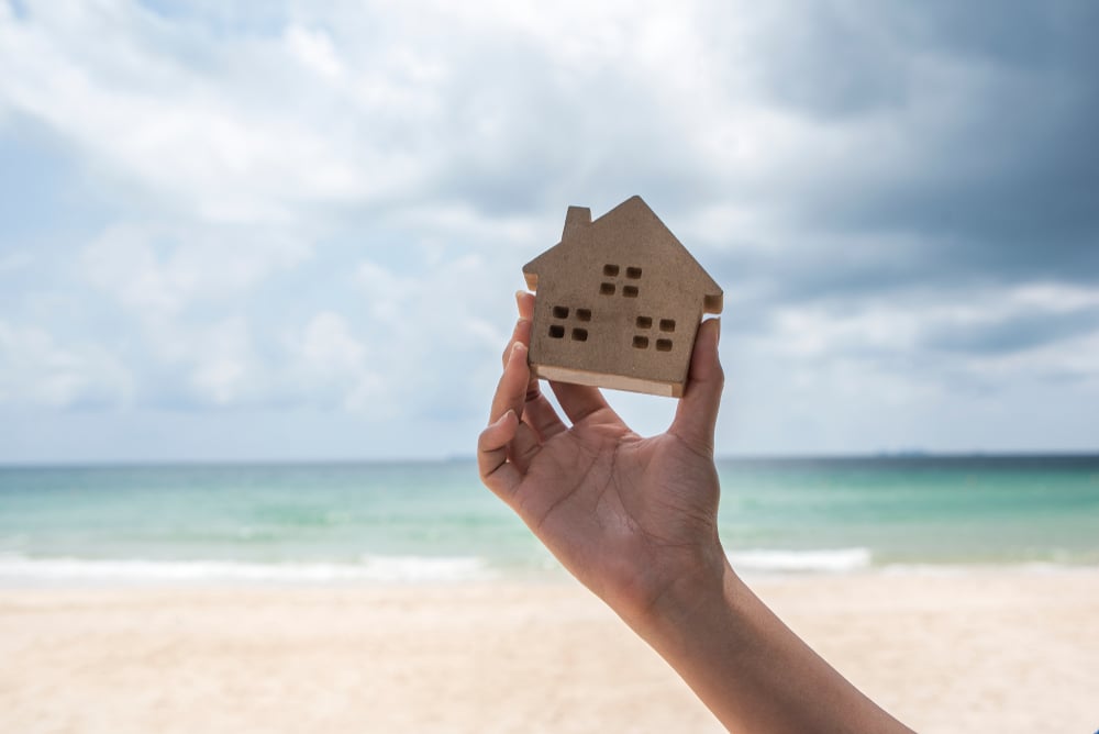 hand holding model of home in front of beach
